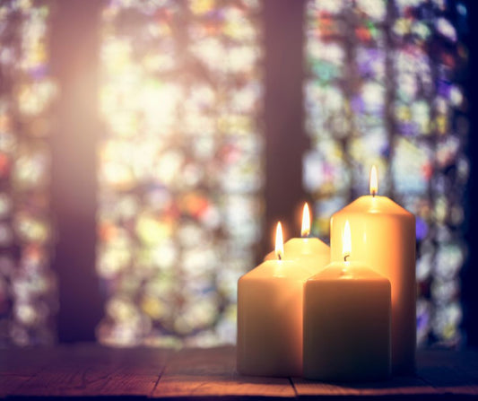 Lit candles in front of softly glowing stained glass windows