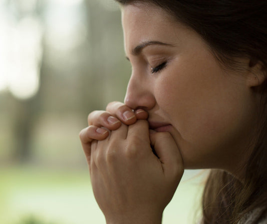 A woman with her eyes closed and hands clasped in prayer near her face