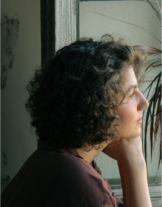 A woman resting her chin on her hand, looking thoughtfully out a window